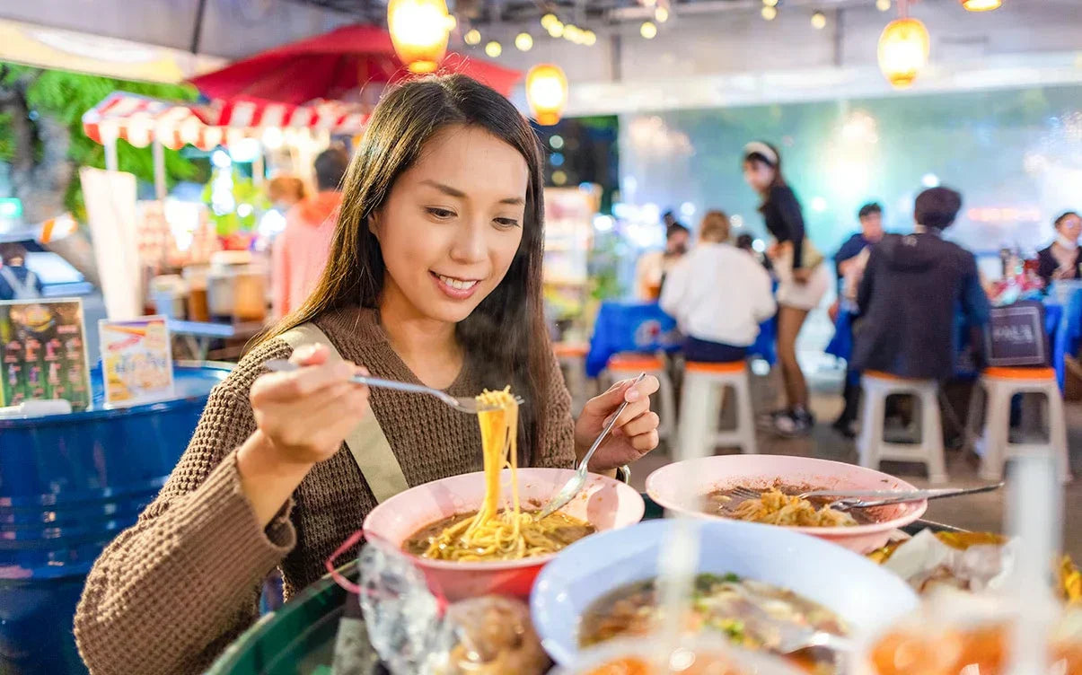 A close-up of a steaming bowl of noodles on a traditional plastic hawker tray, representing the sensory experience of solo dining.