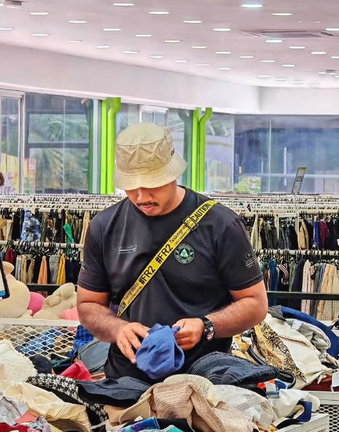 A stylish shopper browsing through colorful racks of vintage clothing and oversized jackets at a popular Kuala Lumpur thrift store.