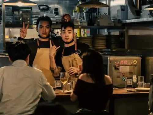 A team of young chefs in their twenties collaborating in the open kitchen at Pilot Kitchen Singapore, preparing creative seasonal dishes.