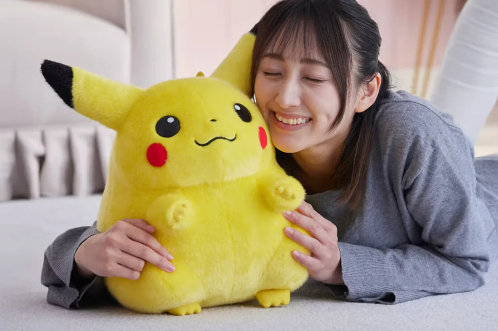 Person holding a large Pikachu plush toy on a bed
